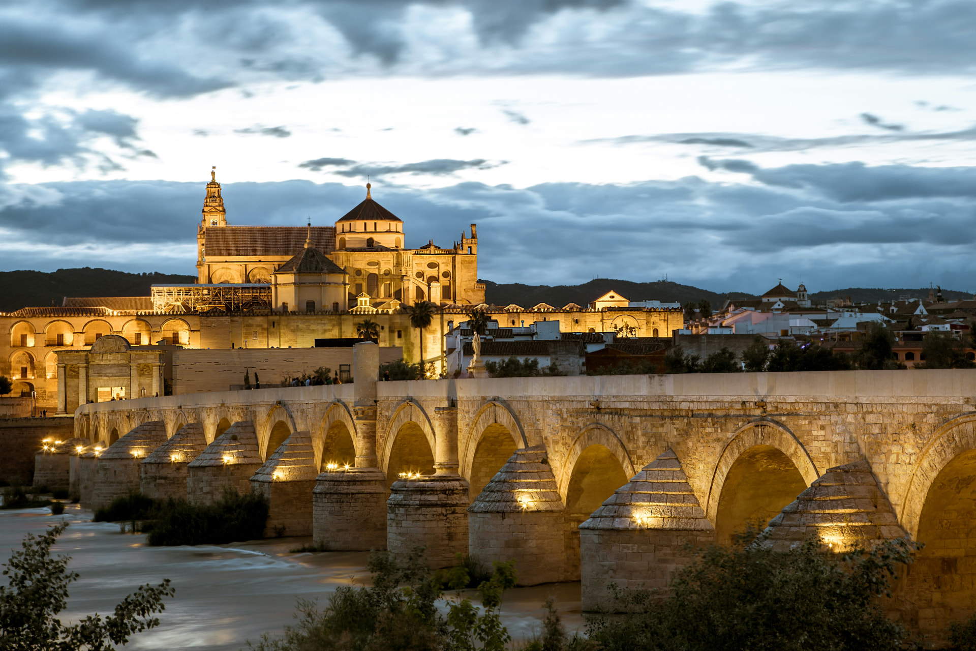 Roman bridge and Mezquita of Córdoba lit up at dusk