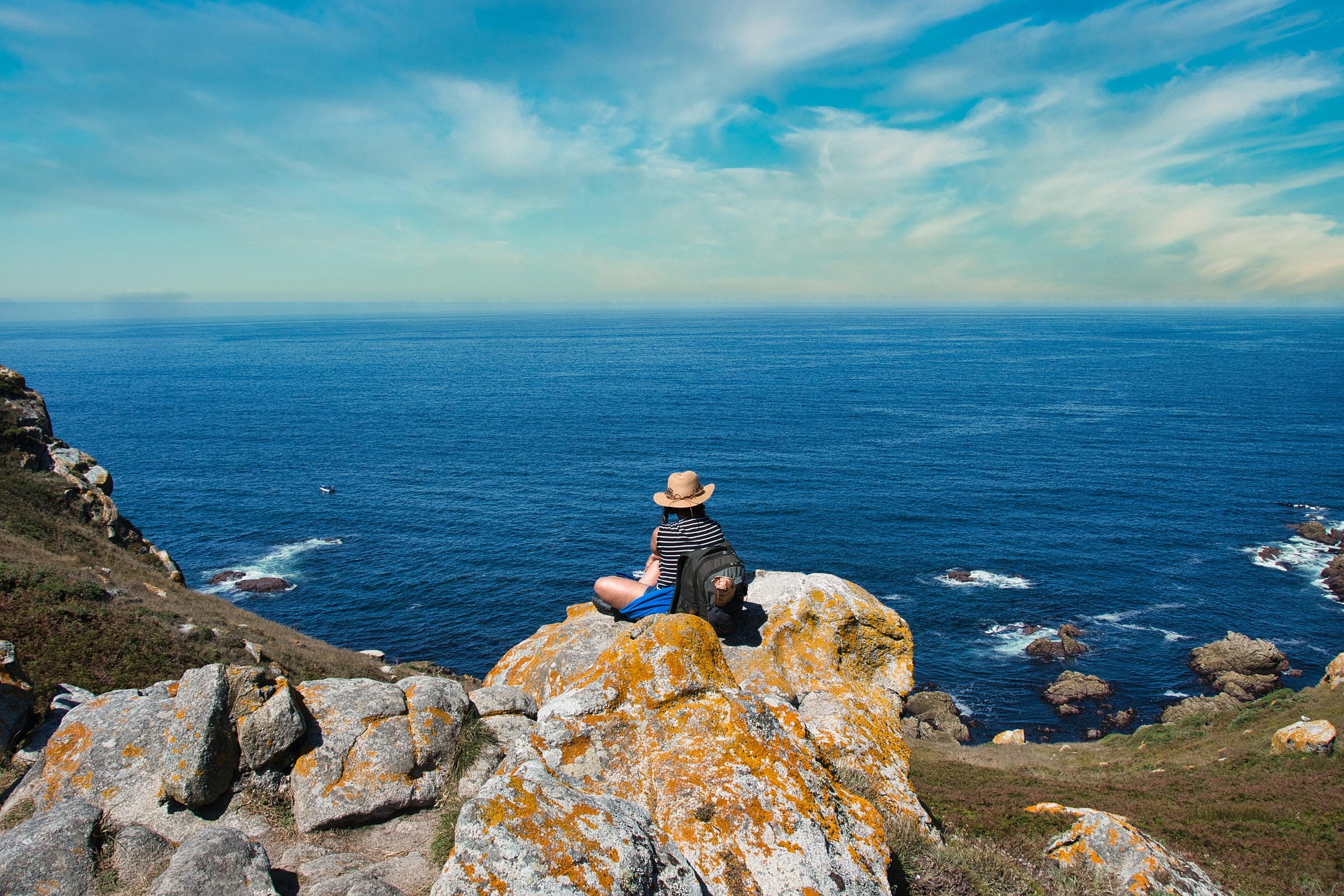 Hiker sitting on lichen-covered rocks above the Atlantic on the Spanish coast