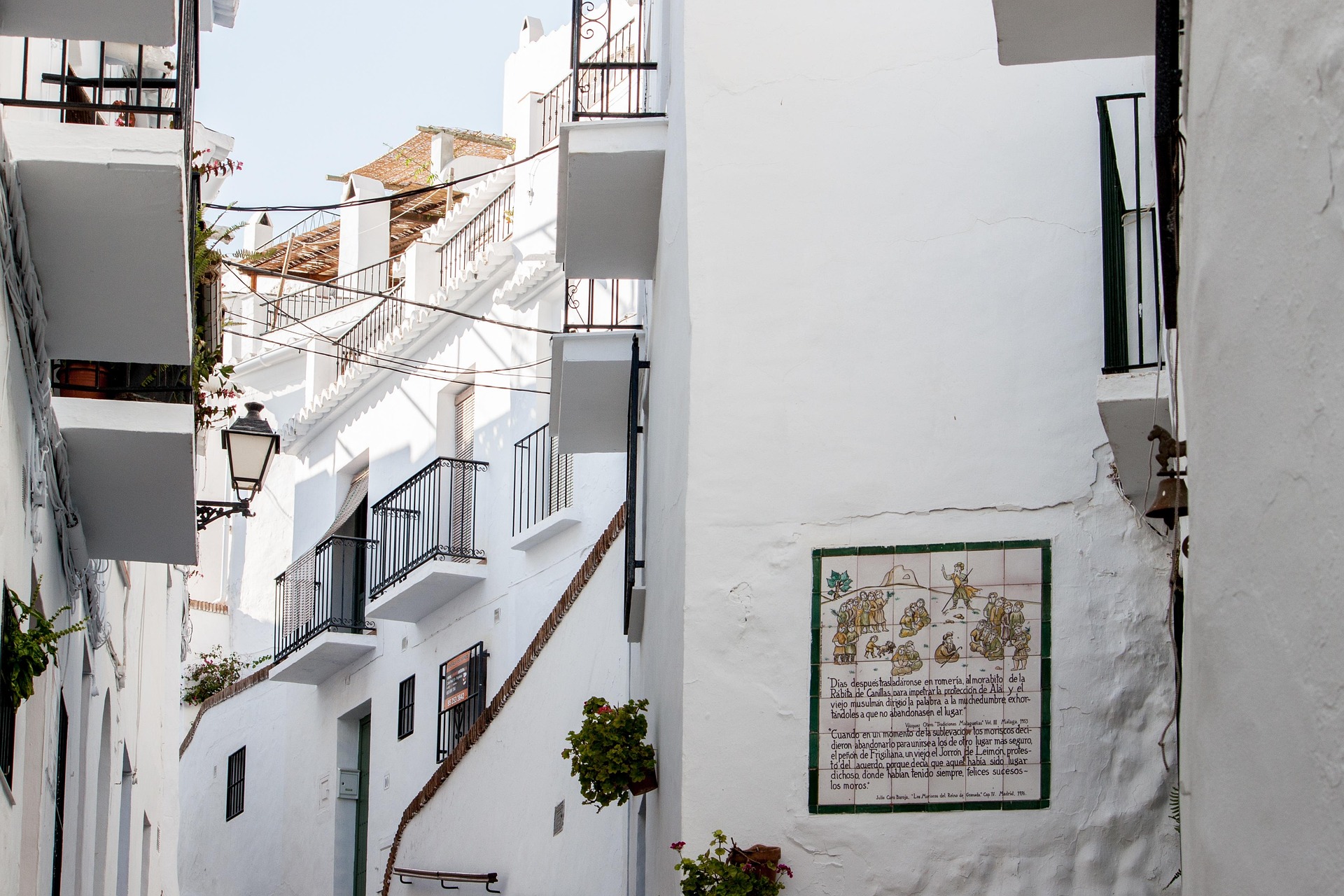 Whitewashed street with balconies and a painted tile mural in an Andalusian village